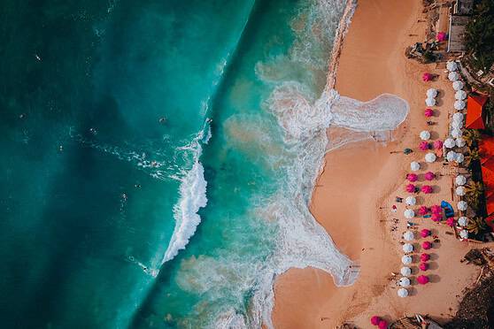 Beach with colorful umbrellas, sunbathers, and clear blue ocean waves.