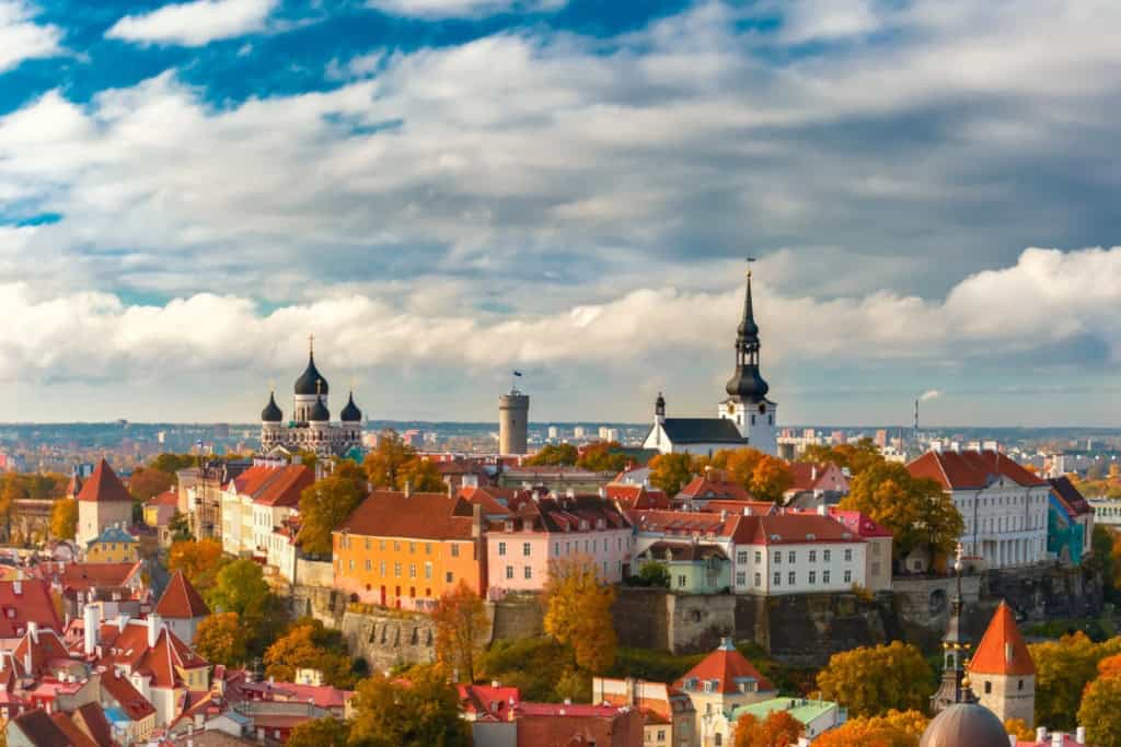 Panoramic view of Tallinn, Estonia, showcasing historic architecture, colorful rooftops, and prominent church spires under a partly cloudy sky.