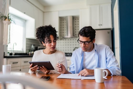 Two professionals discussing insurance options at a kitchen table, reviewing documents and a tablet, in a bright, modern kitchen setting.