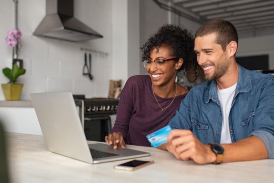 Happy couple using a credit card and laptop in a modern kitchen, highlighting international credit card benefits for living abroad.