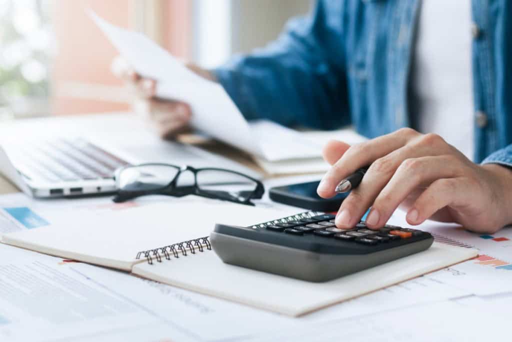 Person using calculator and documents for financial planning, with a laptop and glasses on the table, emphasizing financial advice for expatriates.