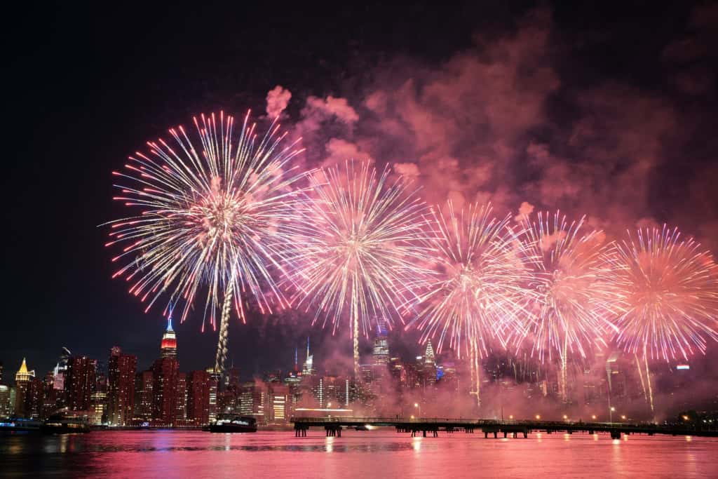 A vibrant display of fireworks illuminating the night sky above a city skyline, reflecting on the water below, celebrating a festive occasion with colorful explosions.