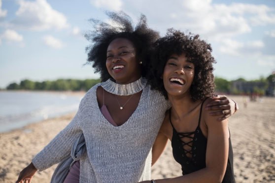 Two women smiling and embracing each other on the beach, highlighting the importance of mental health support for international travelers.