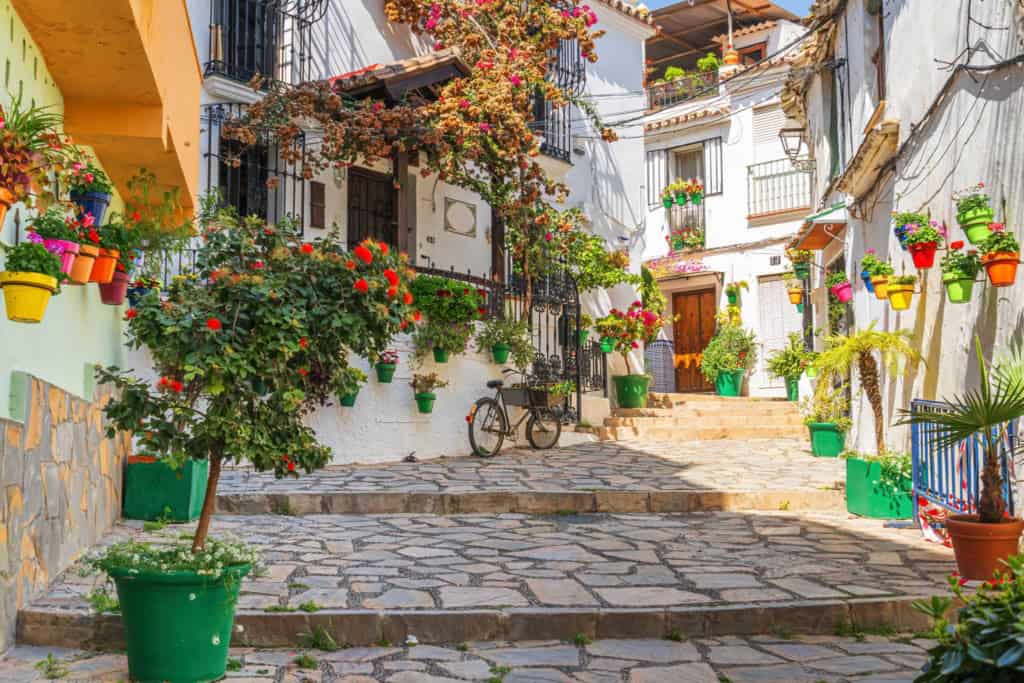 Charming Spanish village street with colorful flowers and potted plants.