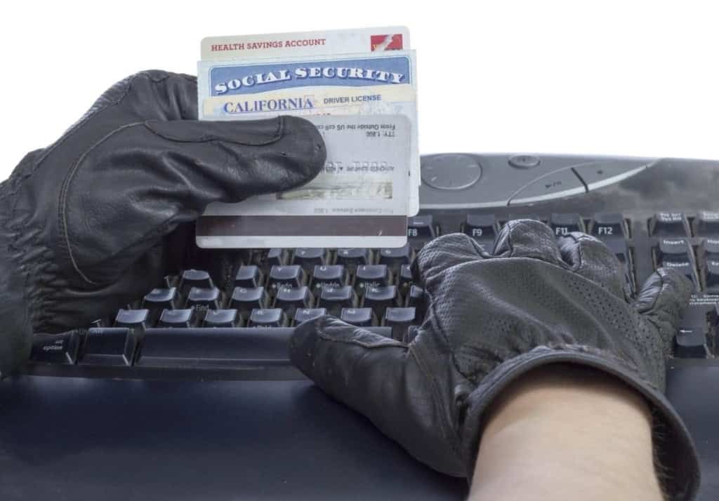 Person wearing black gloves handling a social security card and driver license over a computer keyboard, highlighting identity theft and fraud risks.