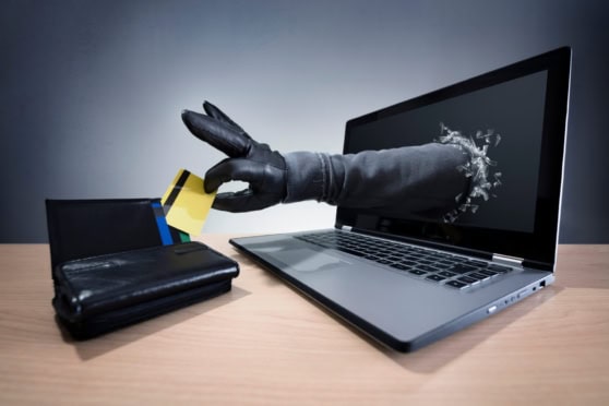 Digital security concept showing a gloved hand reaching through a laptop screen to grab a credit card, symbolizing online financial transactions and cybersecurity risks.