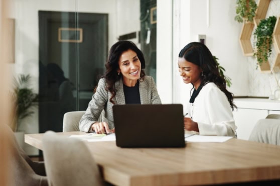 Two women discussing insurance options at a modern office table with a laptop, representing international insurance services for global citizens.