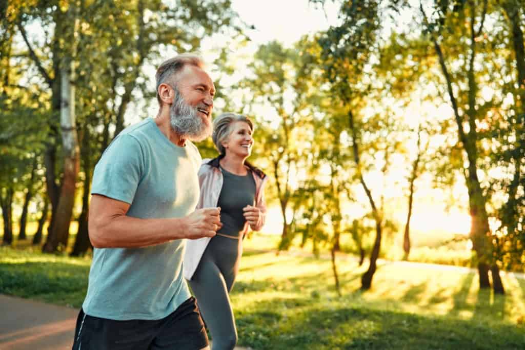 Active seniors jogging in a park with lush trees and warm sunlight, highlighting how good climate and lifestyle are an important part of retirement planning for expats