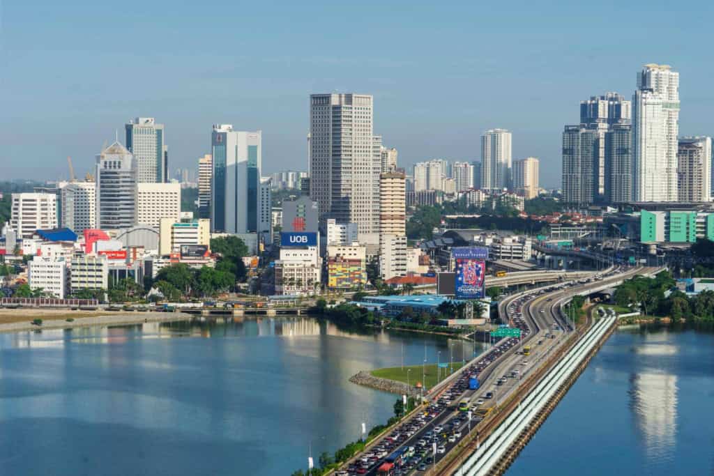 A vibrant cityscape of Singapore featuring tall buildings, a river, and a busy highway, illustrating the urban environment ideal for retirees considering relocating to Malaysia.