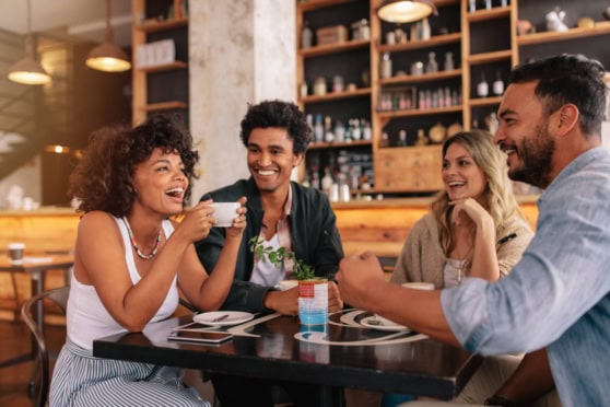 Group of diverse friends laughing and enjoying coffee together at a cozy café, showcasing friendship and social connection.