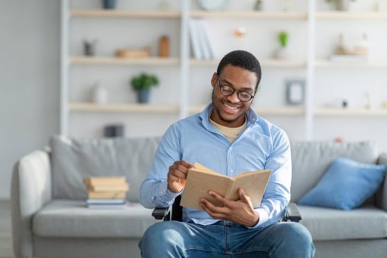 Smiling man with glasses reading a book in a cozy living room setting, representing international insurance services for global citizens.