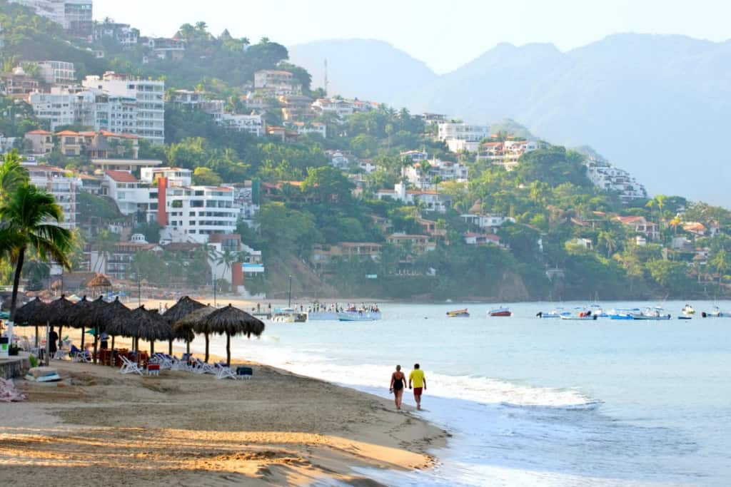 Beachside resort with hillside city view, palm trees, and boats in the water.