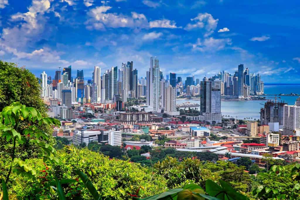 A panoramic view of Panama City showcasing its impressive skyline with tall skyscrapers, lush green hills in the foreground, and a vibrant cityscape under a bright blue sky; one of the best places to retire in Panama
