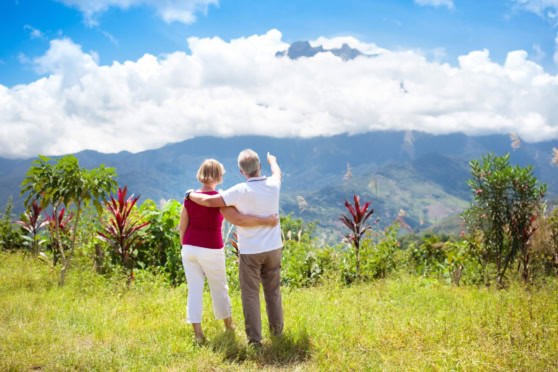An elderly couple enjoying the scenic landscape of Malaysia, with lush greenery and mountains in the background, perfect for retirees seeking a peaceful and beautiful retirement destination.