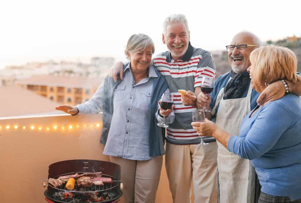 Group of happy seniors enjoying a barbecue on a terrace during sunset, celebrating retirement in Spain with friends and good food.