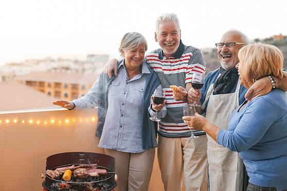 Group of happy seniors enjoying a barbecue on a terrace during sunset, celebrating retirement in Spain with friends and good food.