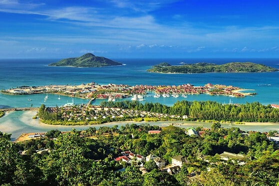 Scenic view of a tropical island with lush greenery, clear blue waters, and a small town along the shoreline, showcasing a beautiful coastal landscape ideal for travel and leisure.