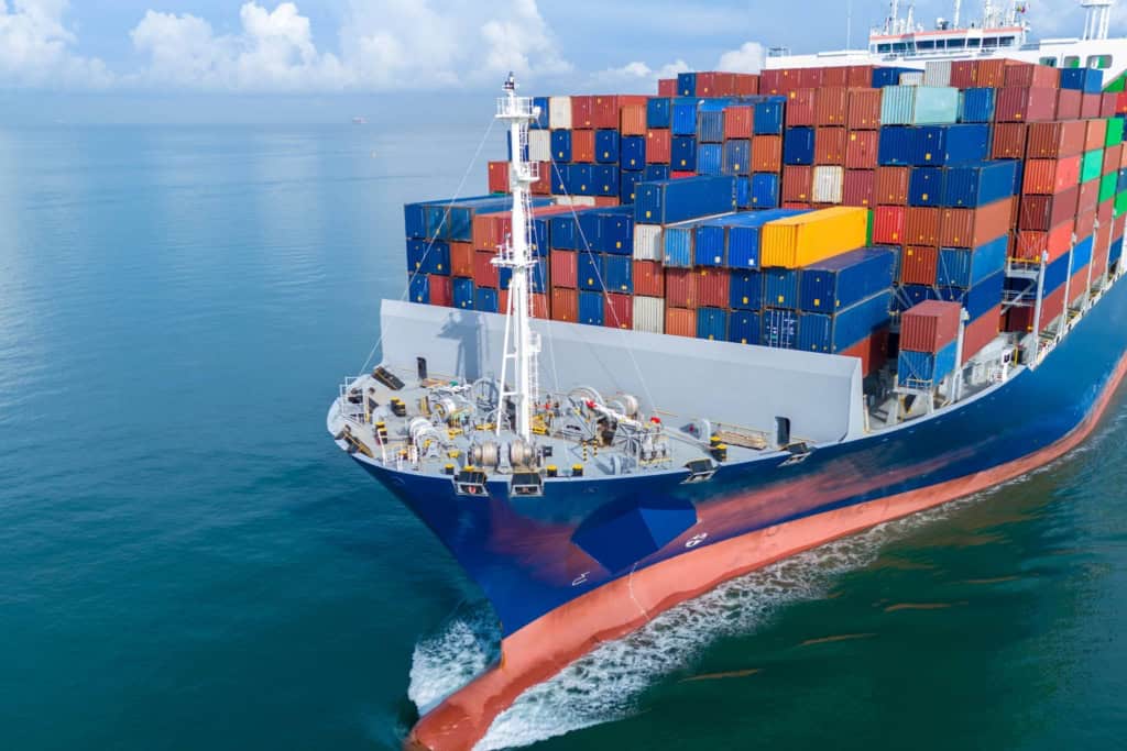 A large container ship sailing through the ocean, loaded with colorful shipping containers, representing international trade and global logistics.