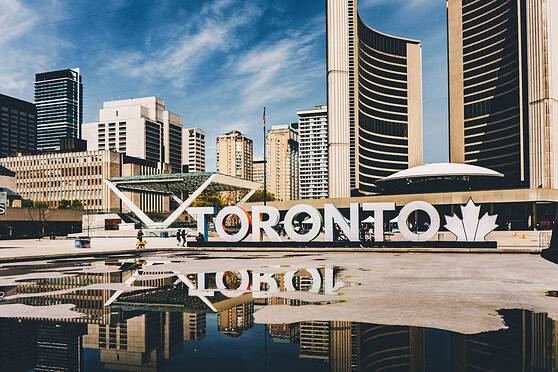 A vibrant cityscape of Toronto featuring tall buildings, clear blue skies, and the famous "TORONTO" sign, highlighting the city's dynamic urban environment for expats living in Toronto.