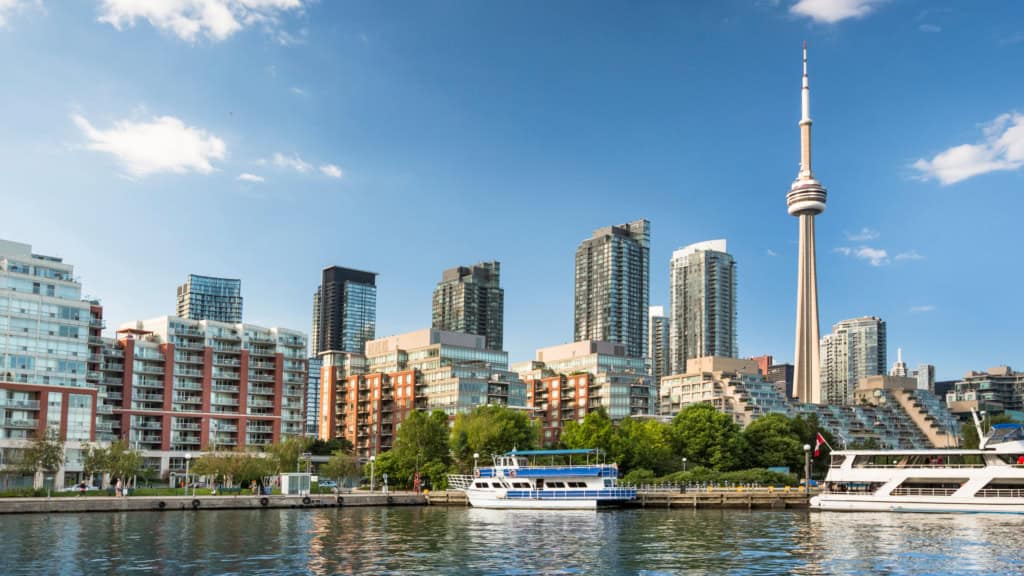 A panoramic view of Toronto's cityscape featuring the iconic CN Tower, modern high-rise buildings, and the waterfront with boats, highlighting the vibrant urban environment for expats.
