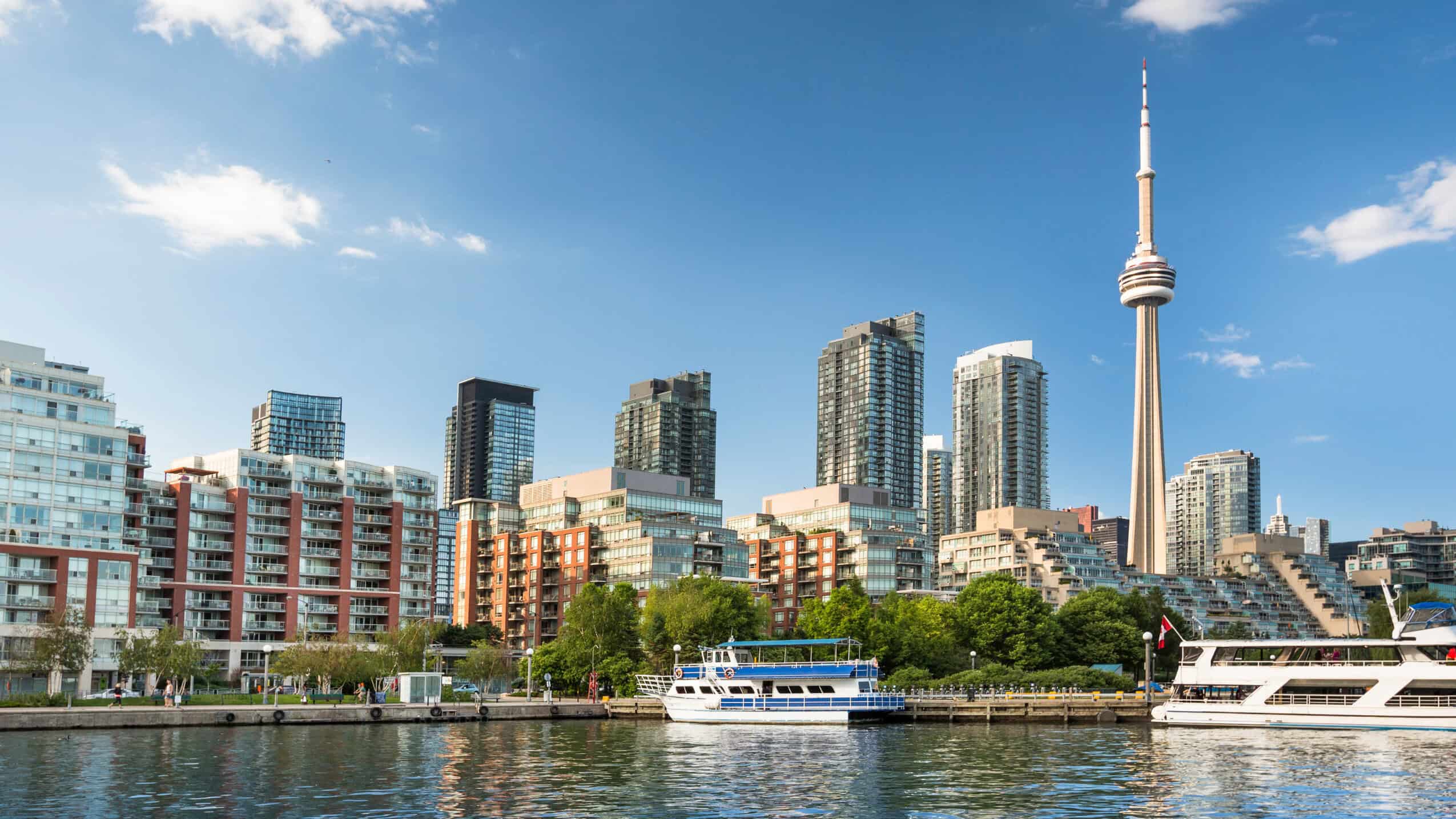 A panoramic view of Toronto's cityscape featuring the iconic CN Tower, modern high-rise buildings, and the waterfront with boats, highlighting the vibrant urban environment for expats.