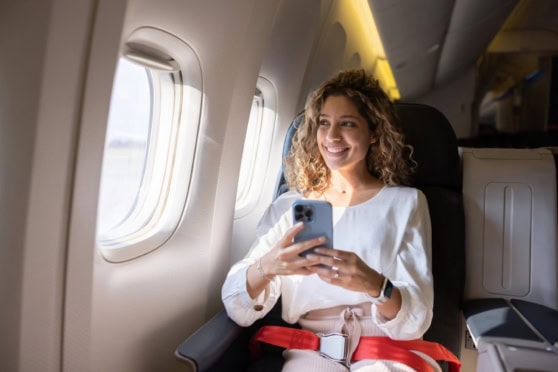 Window seat passenger smiling and using her phone on a plane.