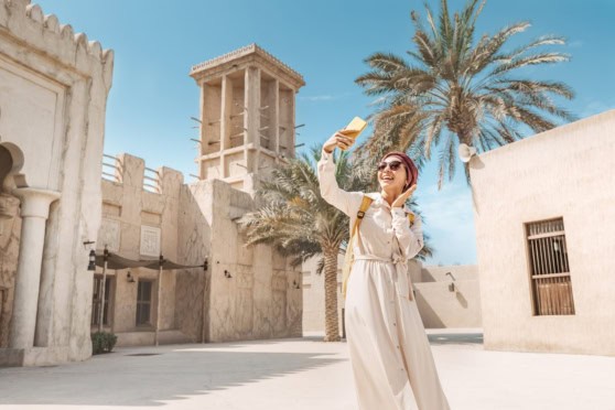 A woman taking a selfie in Dubai's historic district with traditional architecture and palm trees, highlighting the vibrant culture and modern opportunities for work visas.