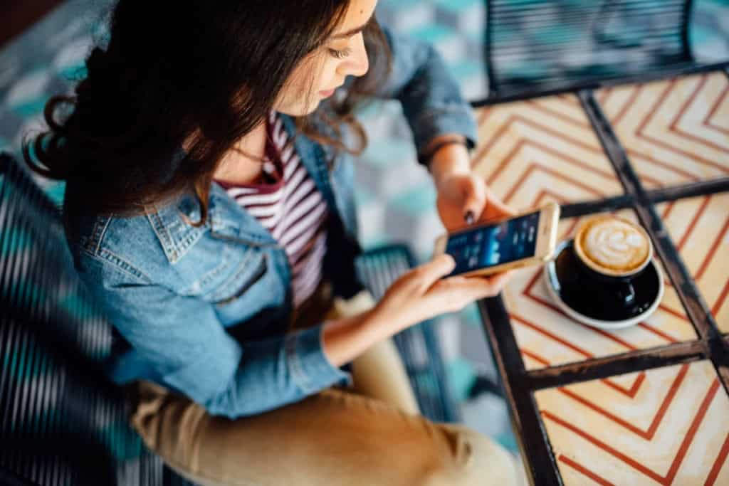 Woman using her smartphone at a café table with a coffee cup, representing international health insurance and global coverage for expatriates and travelers.