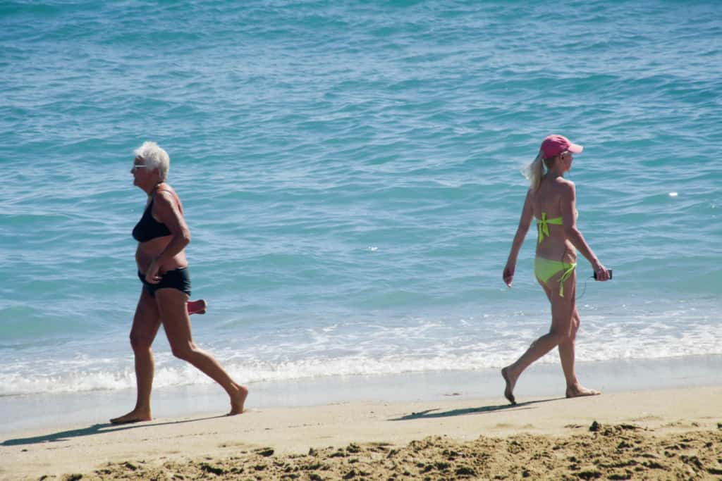 A senior woman and a young woman walking along the beach shoreline in Spain, enjoying the sunny weather and ocean view.