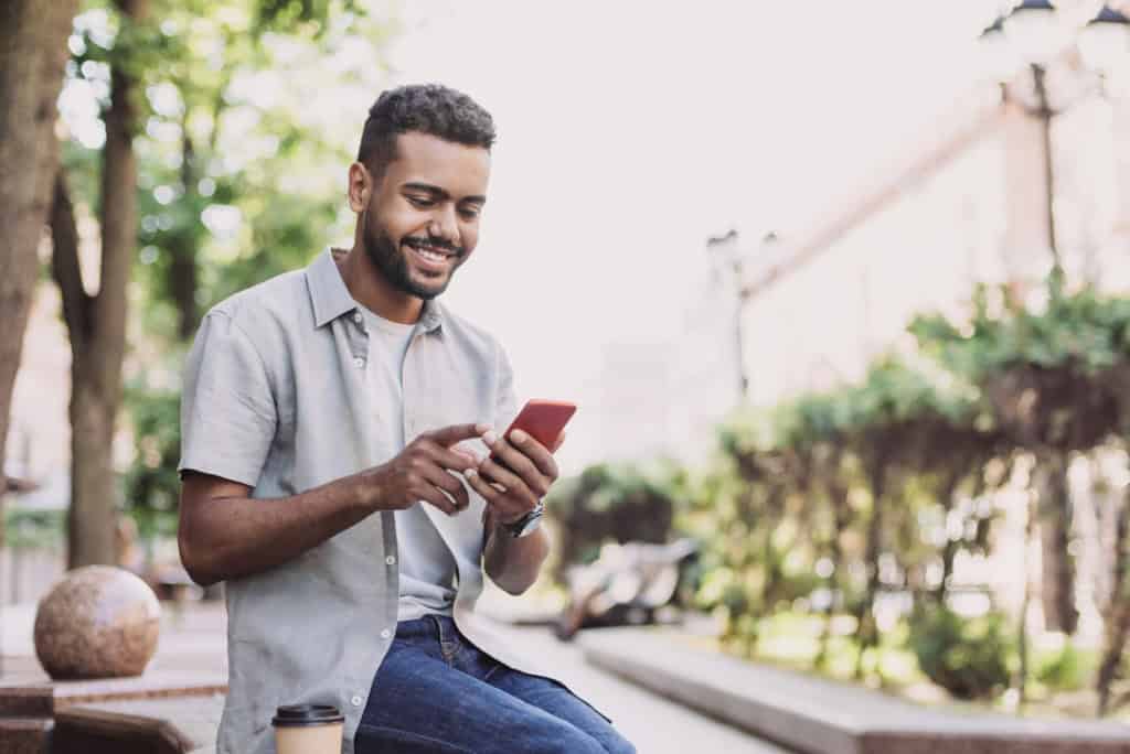Smiling man using smartphone outdoors, representing international travel and expat insurance services.