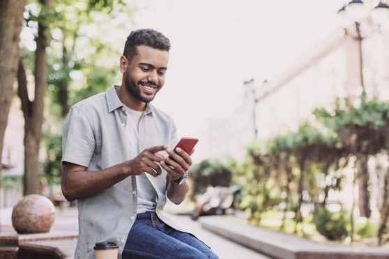 Smiling man using smartphone outdoors, representing international travel and expat insurance services.
