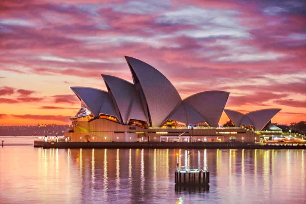 Sydney Opera House illuminated at sunset with vibrant sky reflections on the water.