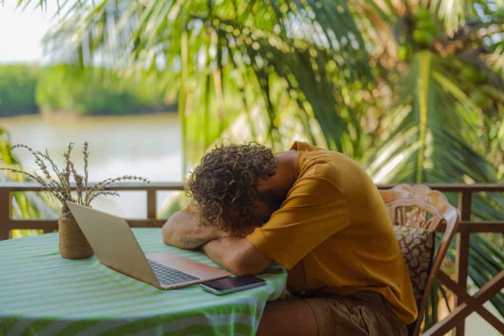 Man in distress with open laptop sitting on the patio, showing the risk of developing remote work burnout when working around the world