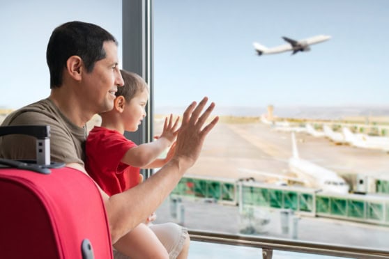 Family enjoying watching an airplane take off at the airport through a large window.