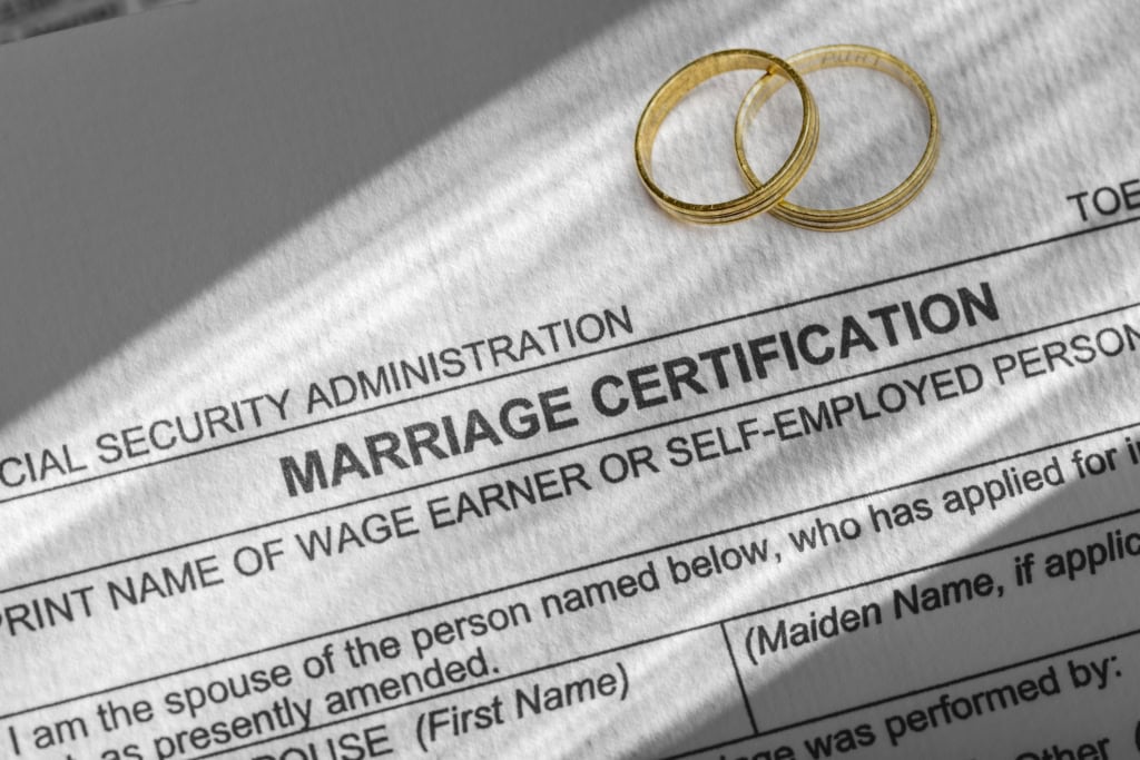 Marriage certificate with two gold wedding rings placed on top, symbolizing marriage and commitment. The document is from the Social Security Administration, indicating official marriage registration and is required when getting married abroad