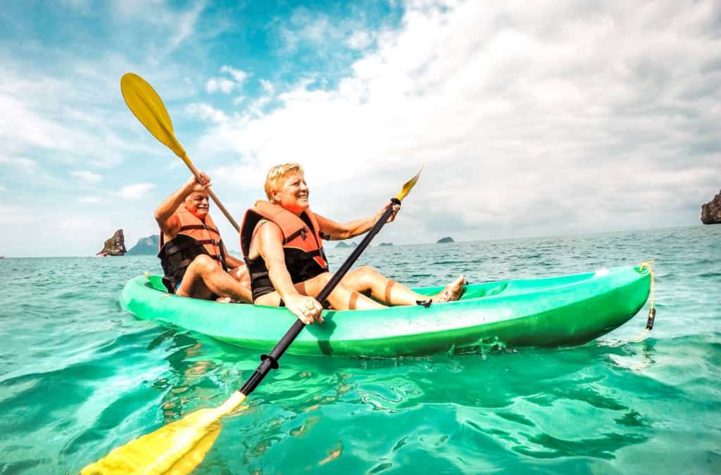 A happy senior couple enjoying retiring in the Philippines, sitting in a kayak on clear, calm ocean waters.