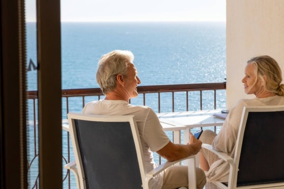 Senior couple sitting on balcony overlooking the ocean, enjoying a peaceful moment and the scenic sea view.