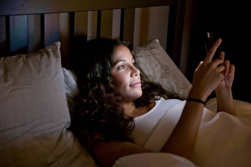 a woman checking her emails on her phone late at night, highlighting the risk of remote work burnout