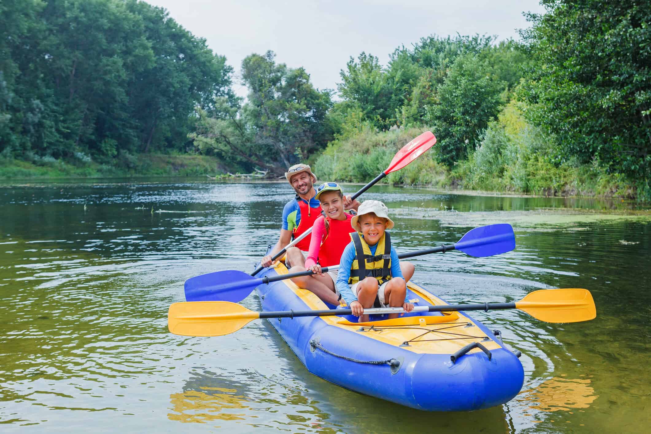 Family kayaking on a river in the United States, surrounded by lush green trees, during a family travel outing.