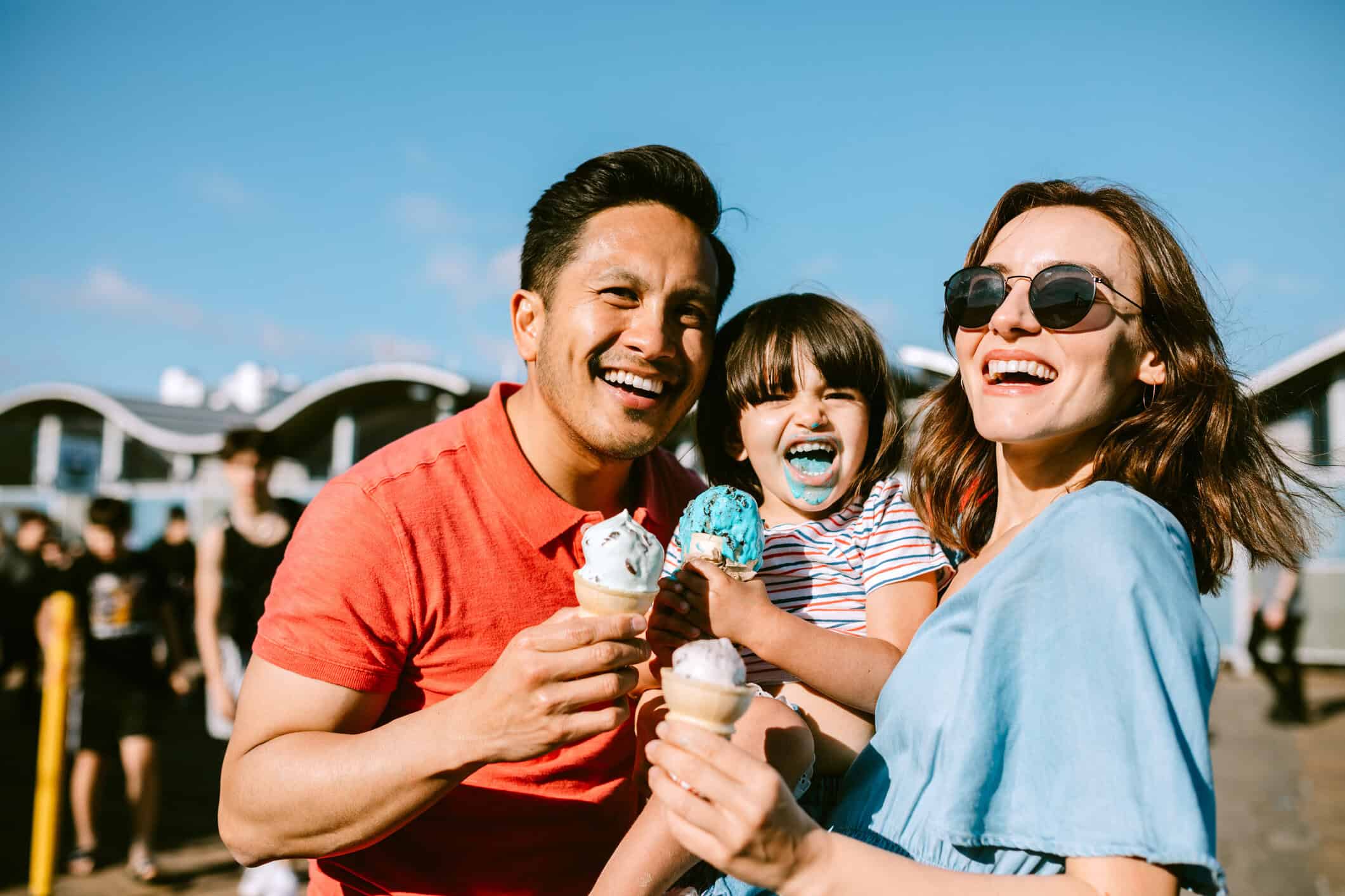 Family enjoying ice cream outdoors in a sunny, coastal city with modern buildings in the background.