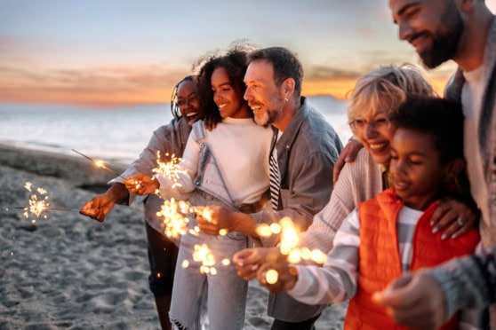 Family celebrating with sparklers on a beach in the United States during sunset, related to family travel insurance.