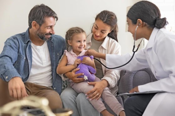 Parents and young daughter visiting a doctor and receiving medical care, showing the importance of international family health insurance for accessing healthcare abroad.