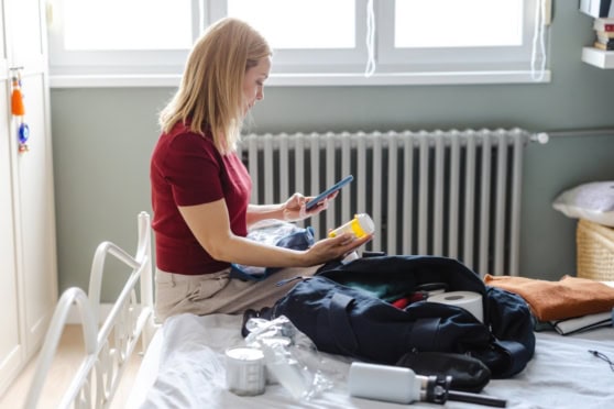 A woman checking medication while packing for a trip, illustrating travel insurance for pre-existing conditions.