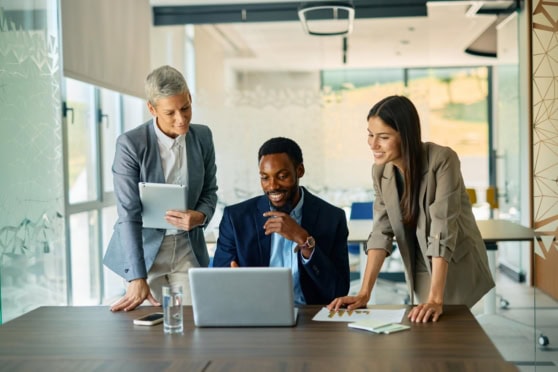 Three employees gathered around a laptop discussing international group insurance in a workplace