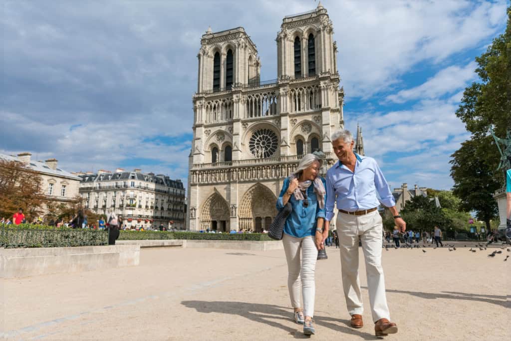 Couple walking in front of Notre-Dame Cathedral in Paris, France, on a sunny day.