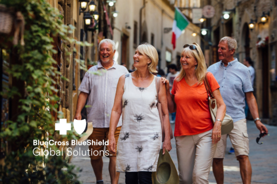 Group of mature tourists walking through a historic Italian street with flags and outdoor cafes.