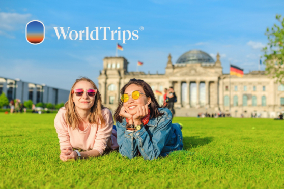 Two young women lying on the grass in Berlin, Germany, with the Reichstag building in the background, enjoying a sunny day.