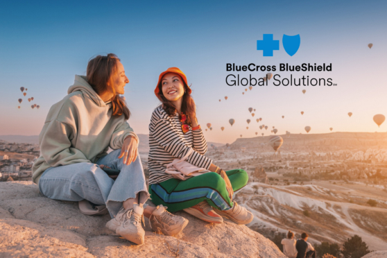 Two women sitting on a rock in Cappadocia, Turkey, watching hot air balloons at sunset.