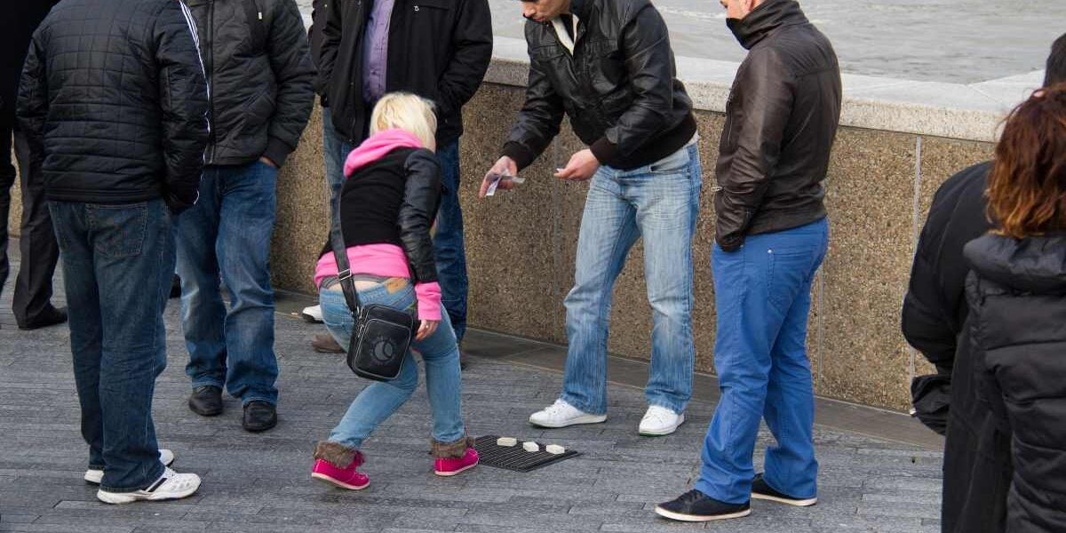 illegal-shell-game-gambling a female tourist falling victim to one of the shell game travel scams in London, UK