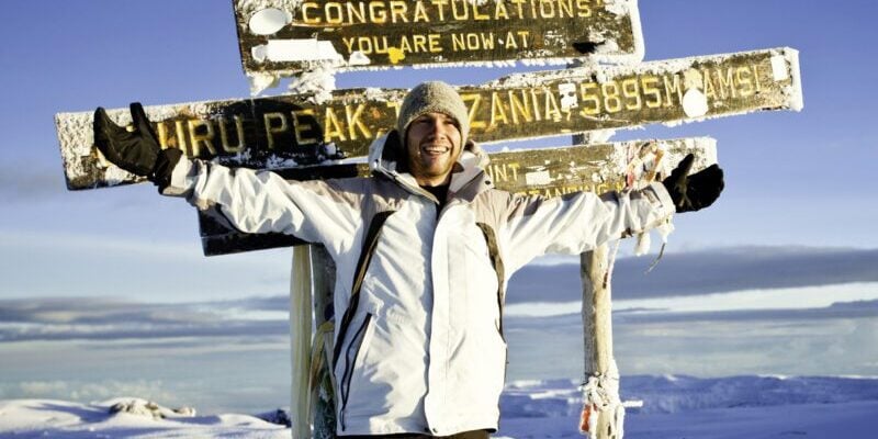 a man standing at the top of Mount Kilimanjaro, highlighting the importance of securing medical evacuation insurance when visiting remote locations